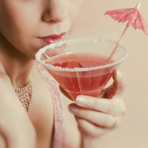 Beautiful young vintage 1920s woman with headband and flapper dress drinking a cocktail
